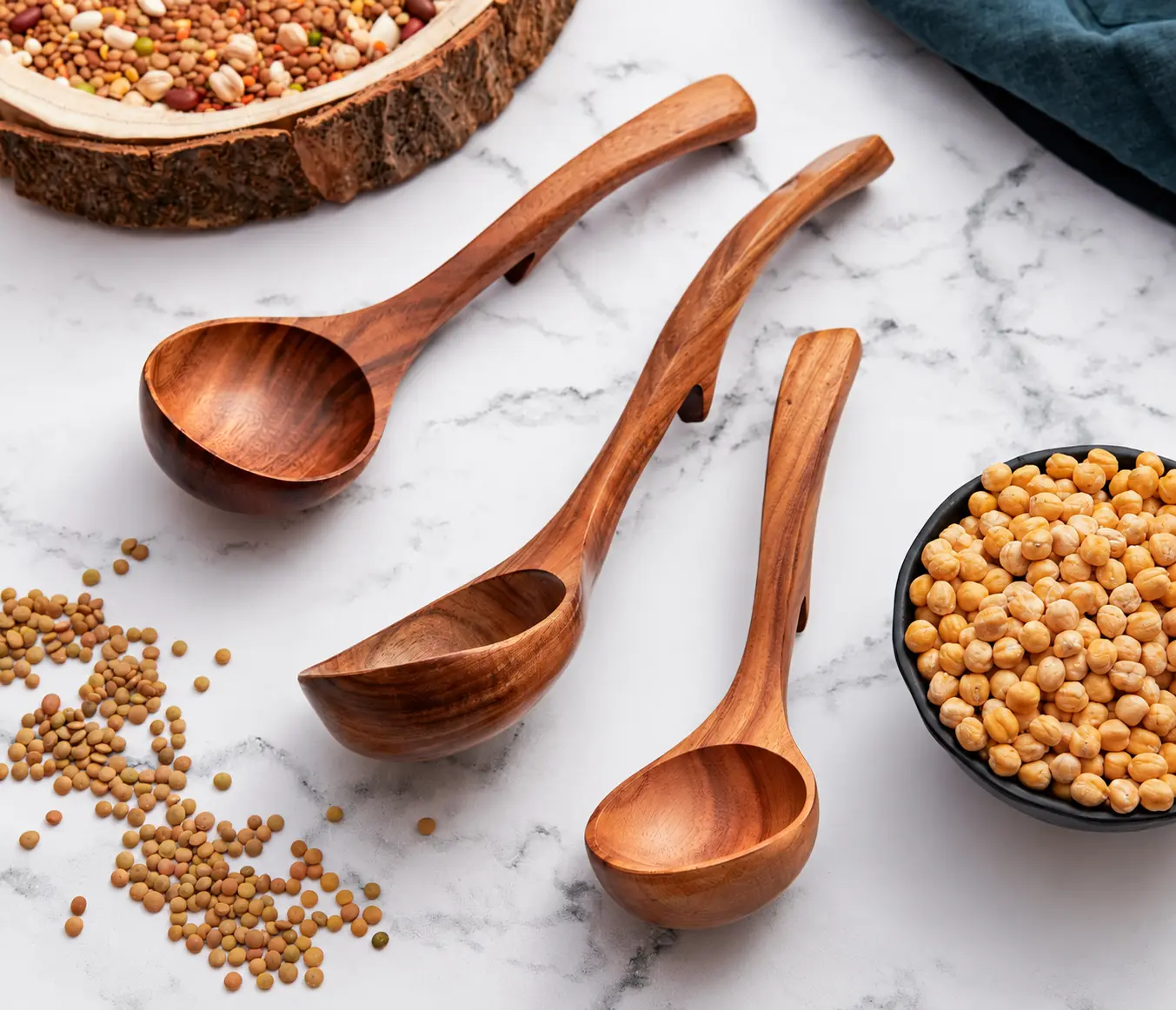 Three ladle spoons with curved handles and back hooks arranged on a marble surface