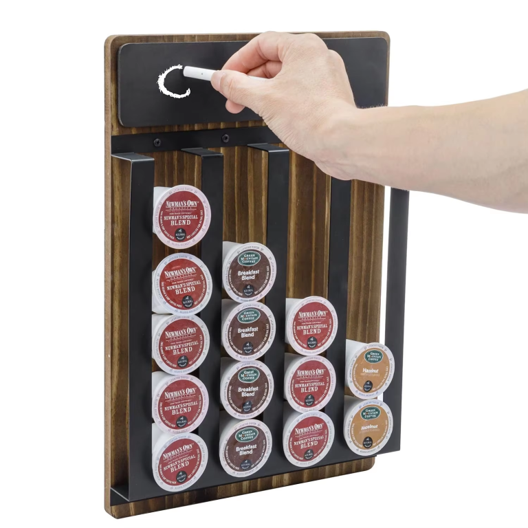 Hand writing with chalk on the top board of a wood-toned coffee pod organizer with four black vertical channels holding pods