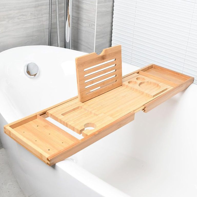 Empty bamboo bathtub tray with a notched slotted upright panel, circular and rectangular recesses and extended end trays across a white bathtub