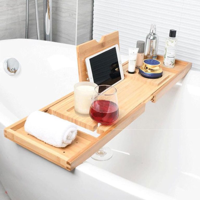 Bamboo bathtub tray with an upright slotted panel and extended end trays, pictured across a bathtub with a tablet, stemmed glass, towel and toiletries