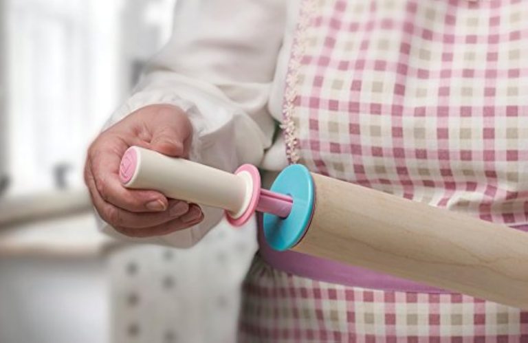 Hand holding the cream handle beside the pink spindle and turquoise thickness ring of a wooden rolling pin