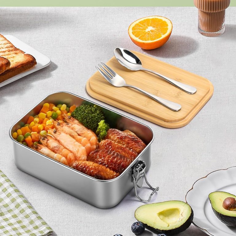 Stainless steel bento box with food inside and a bamboo lid beside it holding a spoon and fork