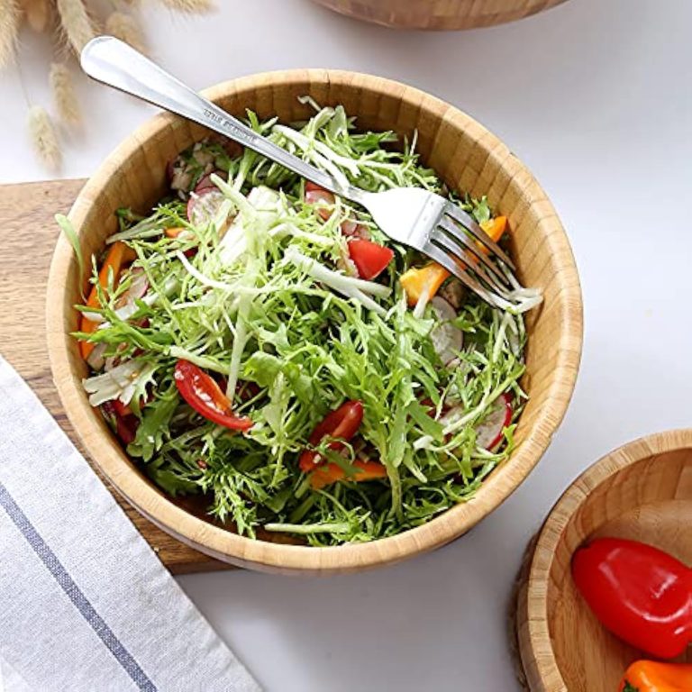Round bamboo salad bowl filled with leafy greens and a fork resting across the rim