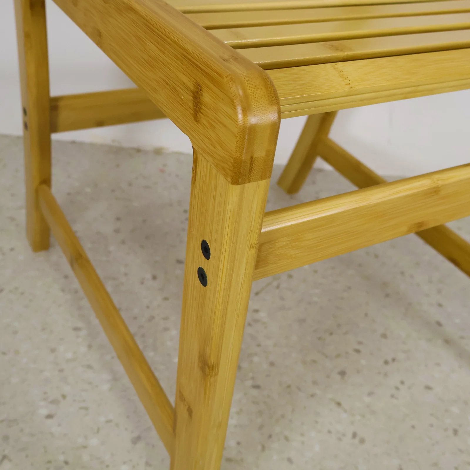 Close-up of the rounded bamboo chair frame joint beside the slatted seat.