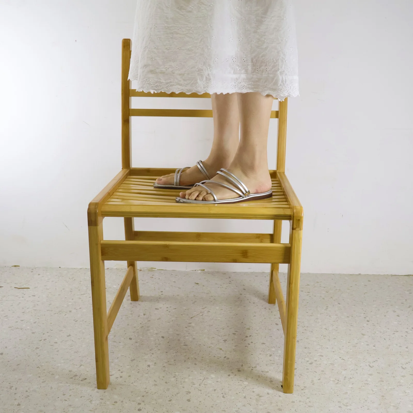 Adult standing on the seat of an adult-size bamboo chair during an informal workshop demonstration.