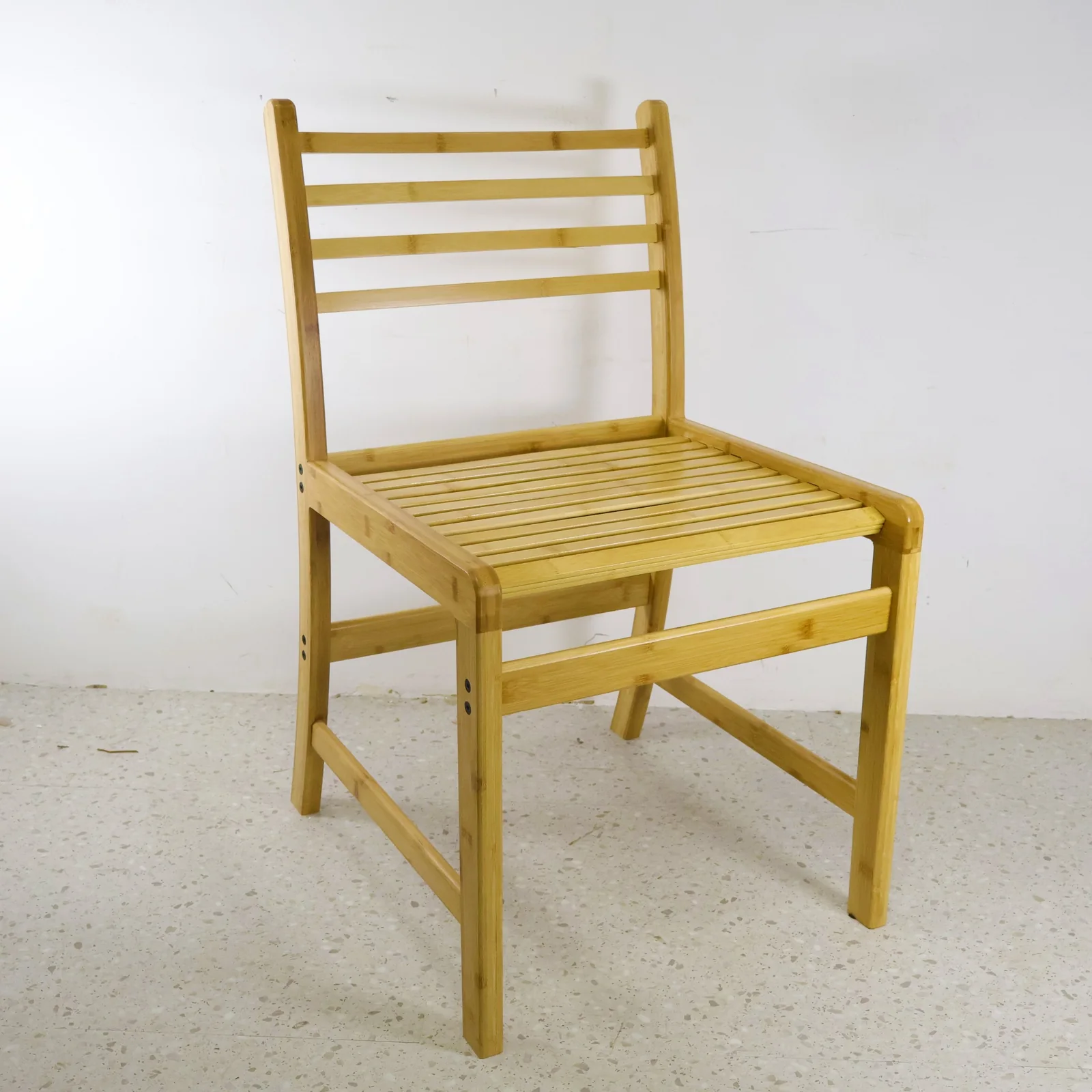 Three-quarter view of a natural bamboo chair with a slatted seat and ladder back.