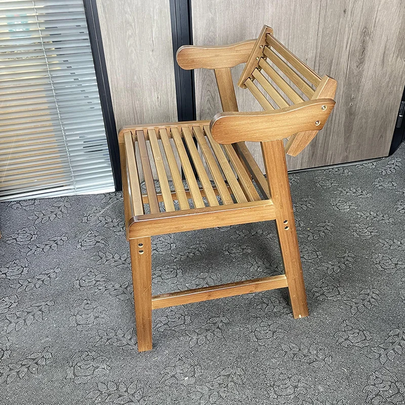 Side three-quarter view of a warm brown bamboo armchair with curved arms, open slats, and a compact upright frame.
